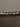 A close-up of a textured, hammered silver metal surface, possibly a frame edge or decorative trim, resting on a dark brown wooden surface against a neutral gray background.