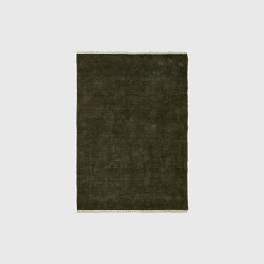 A dark olive green rectangular rug with a textured, hand-woven appearance and subtle cream-colored fringe on the top and bottom edges, shown against a plain light gray background.