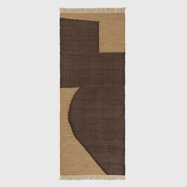 A rectangular, handwoven area rug featuring abstract geometric shapes in tan and chocolate colors with a fringe on the bottom.