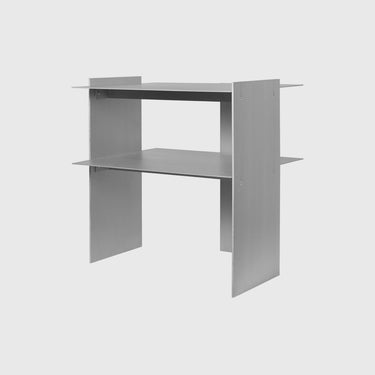 A minimalist two-tier metal desk with a matte gray finish, shown from a three-quarter angle against a light gray background.