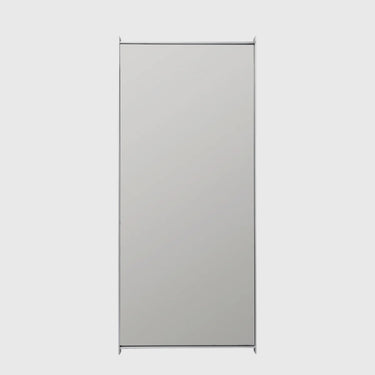 A tall, rectangular wall mirror with a slim silver frame, shown against a solid light gray background.