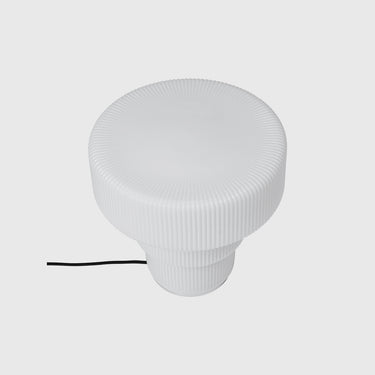 A white ribbed circular lamp shade or diffuser with a short black power cord, shown on a light gray background.