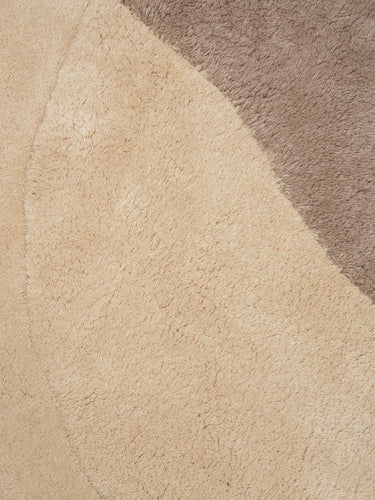 Close-up of a plush shag rug showing a large warm beige section and a smaller taupe-brown section.