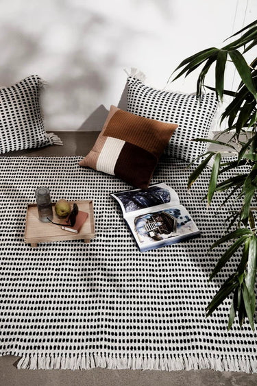 Decorative pillows on a patterned rug with a plant in the corner
