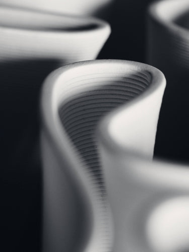 Abstract close-up of sculptural white curved objects with layered ridges, photographed in monochrome against a dark background.