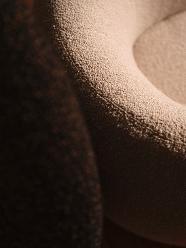 Close-up of a textured beige upholstered chair or cushion with a dark brown textured surface partially visible in the foreground.