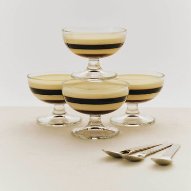 Four glass dessert bowls with striped dessert on a light surface with two spoons.