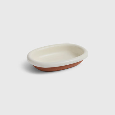 An oval ceramic dish with a glossy off-white glazed interior and a matte terracotta-colored exterior, shown on a light gray background.