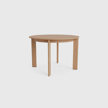 A round light oak dining table with four tapered legs, shown from a low angle against a light gray background.