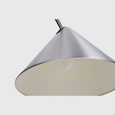 A close-up of a modern pendant light fixture with a brushed silver metal cone shade and a warm cream-colored interior, suspended by a black cord against a light gray background.
