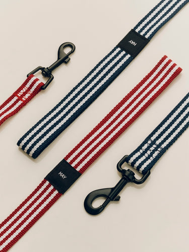 Striped dog leashes in red, white, and blue with black metal clips on a beige background.