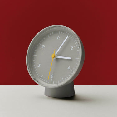Gray clock with white hands and a yellow second hand on a red background