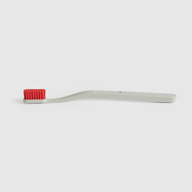 White toothbrush with red bristles on a light grey background