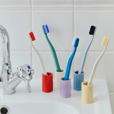 Colorful toothbrushes in holders on a bathroom counter with a tiled wall background.