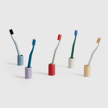Set of five toothbrushes with colorful holders on a light grey background