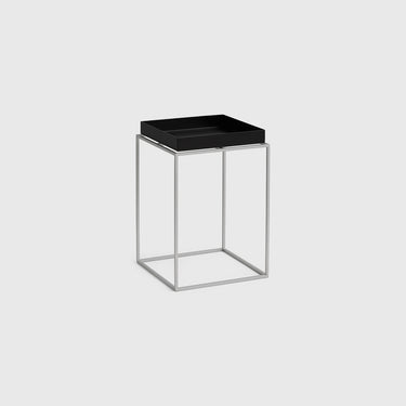 A modern side table featuring a square black tray top mounted on a slim, open cube frame made of silver-toned metal, set against a solid light gray background.