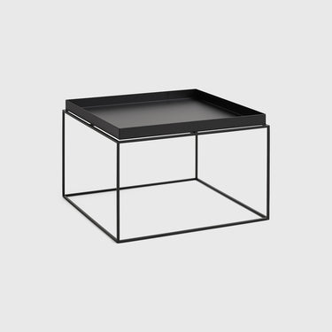 A minimalist square side table featuring a light black tray on top of a thin, open-frame metal base in a matching black tone, set against a solid light grey background.