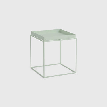A minimalist side table with a square tray top and an open cube frame base, finished in a pale sage green color, set against a light gray background.