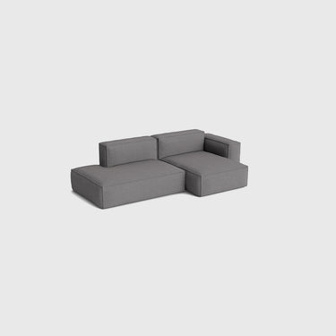 A modern modular sectional sofa in dark grey fabric, shown from a three-quarters perspective against a solid light grey background.