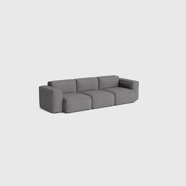 A modern modular three-seater sofa upholstered in dark grey fabric, shown from a three-quarters angle against a solid light grey background.