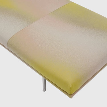 Close-up of a modern upholstered bench or ottoman with a split color-blocked design in pale yellow and cream, supported by slim metallic legs.