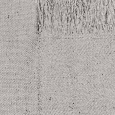 Detail of a natural wool rug with a geometric pattern, featuring long panels and tassels on the sides