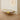 A modern low-profile daybed with a white and yellow abstract patterned cushion, supported by slim metal legs, set in a minimalist room with light wood flooring and a warm glowing circular wall light.
