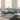 A light blue sectional sofa with a chaise lounge in a bright, modern living room with cream walls, a gray and black rug, and a marble-top side table.