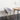A modern chair with a gray upholstered seat and a beige oak frame, with four legs, placed next to a round wooden table with a vase of flowers on it, set against a white wall on a dark floor.