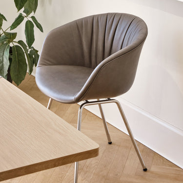 A modern chair with a chrome frame and beige upholstered seat, featuring a quilted backrest, positioned next to a wooden table and a plant.
