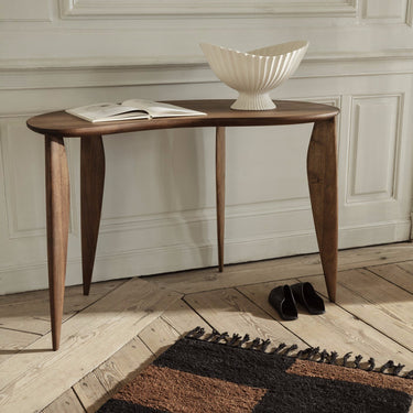 Interior image of a walnut curved desk in a room with a rug, a book and a centrepiece.